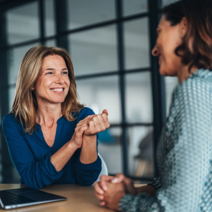 Zwei Frauen sitzen an einem Laptop und lächeln sich an